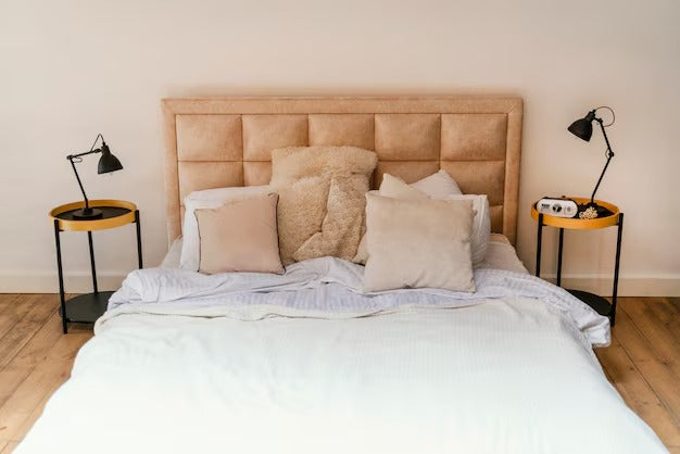 Bed with beige ottoman bed, white linens, and pillows, flanked by black side tables.