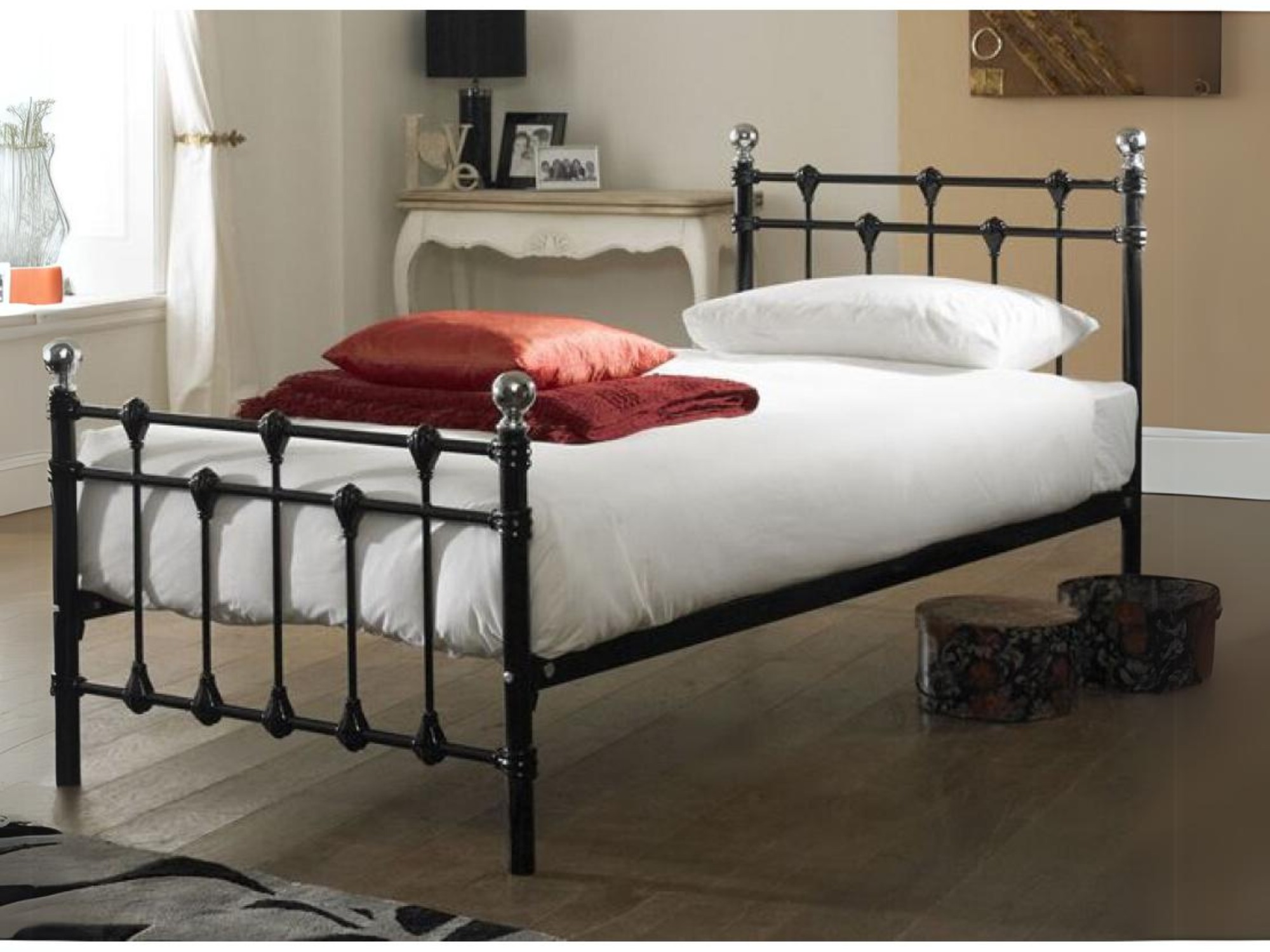 Black metal bed frame with white bedding and red blankets in an elegantly decorated room.