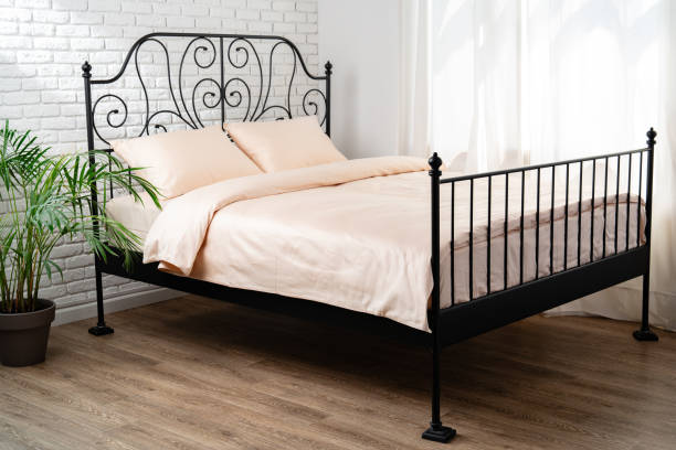 Black metal double bed frame with beige bedding and ornate headboard.