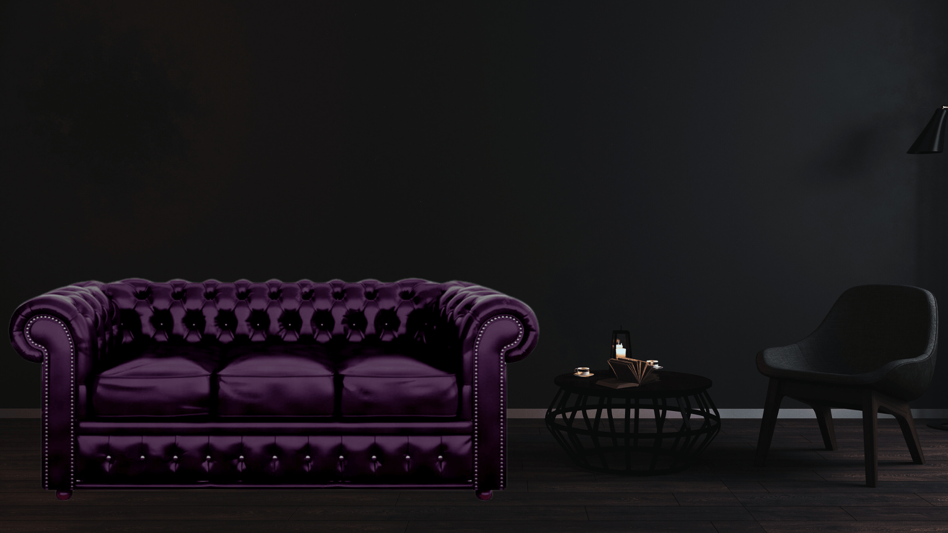 Dark room with a purple Chesterfield sofa bed, a round wooden coffee table, and a black chair.