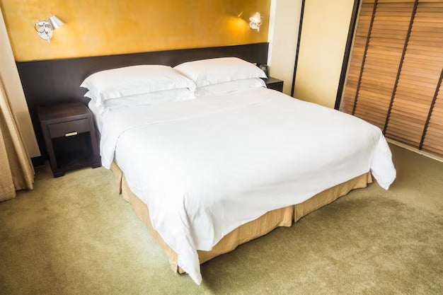 Double bed with white drawers, wooden headboard, and nightstands against a mustard wall.