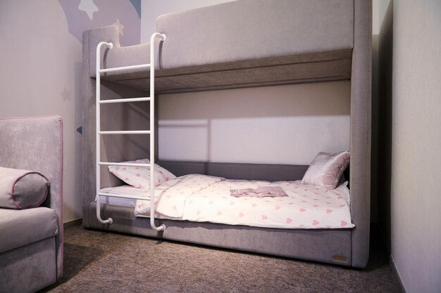 Gray upholstered double bunk bed with a white ladder and pink heart-patterned bedding.