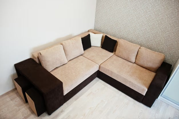 L shaped sofa bed in beige and dark brown with multiple cushions in a room corner.