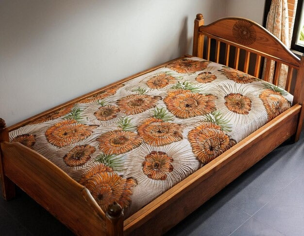 Oak single bed with floral-patterned quilt in a sunlit room.