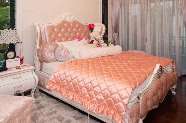 A luxurious bedroom with a princess bed, featuring a tufted headboard and satin bedding.