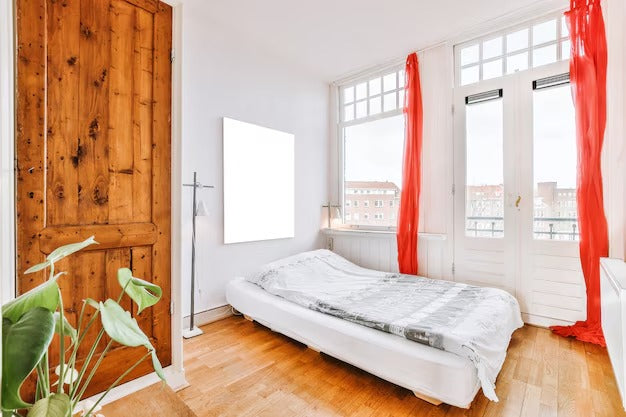 Minimalist bedroom with a single white bed frame and large windows with red curtains.