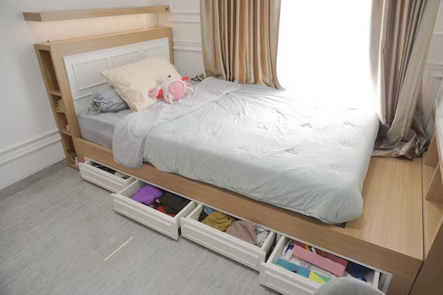 Single bed with storage drawers underneath, gray bedding, and a window with beige curtains.