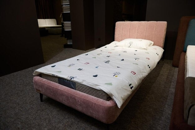 Single floor bed with a pink frame and white duvet in a dimly lit room.