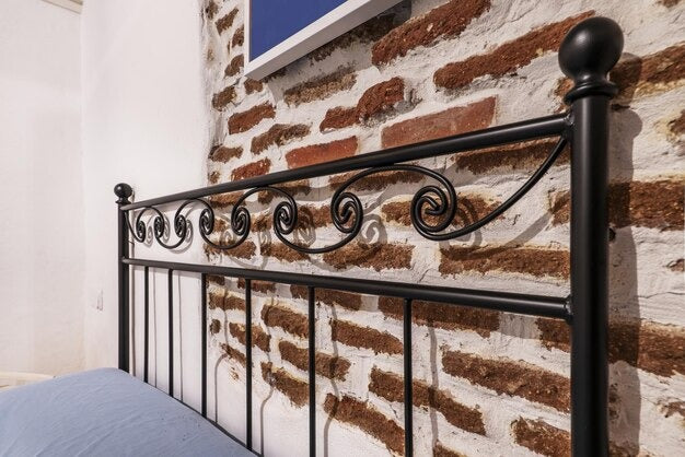 Close-up of a decorative black super king metal bed frame headboard with scrollwork against a brick wall.