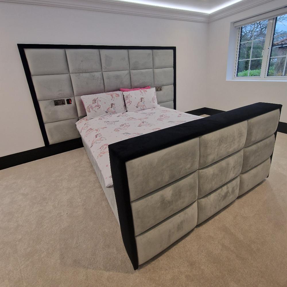 Modern bedroom with tall headboard bed and footboard in gray and black upholstery, and white bedding with pink designs.