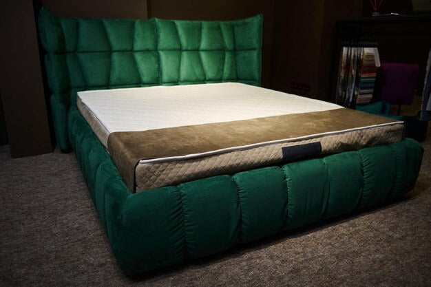 Luxurious green velvet sofa bed with a tufted headboard and a brown quilted cover.