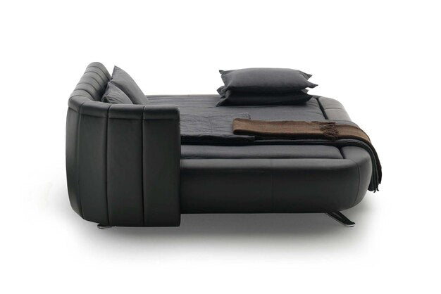 Black couch converted into a bed with pillows and a blanket.