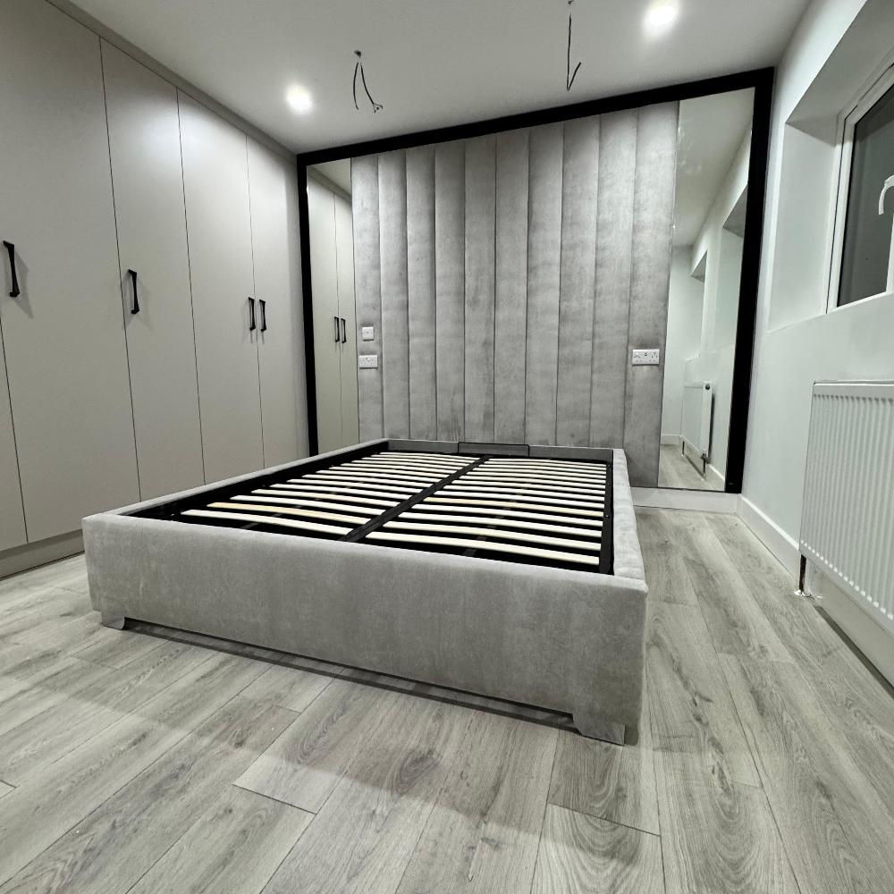 Minimalist bedroom with grey upholstered luxe wall panel bed frame and built-in wardrobes.

