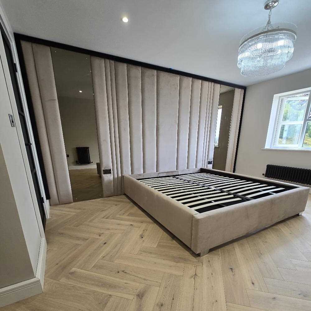 A side angle of the Royal wall panel bed with its distinctive vertical paneled wall feature. The design showcases a modern platform base, elegant crystal chandelier, and light oak herringbone flooring, accented by integrated mirror panels.