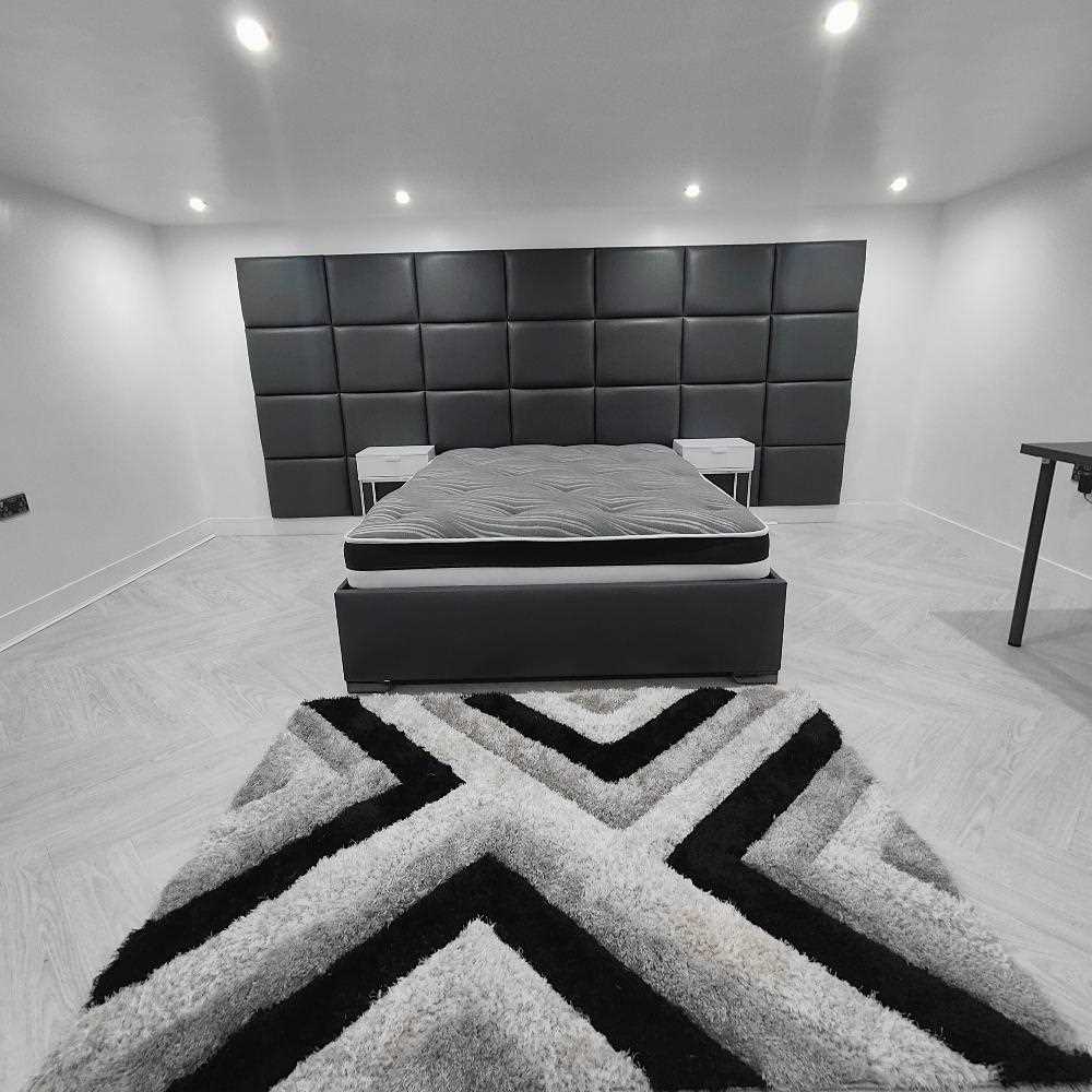 A minimalist bedroom with a dark grey panel headboard, white nightstands, and a geometric rug.