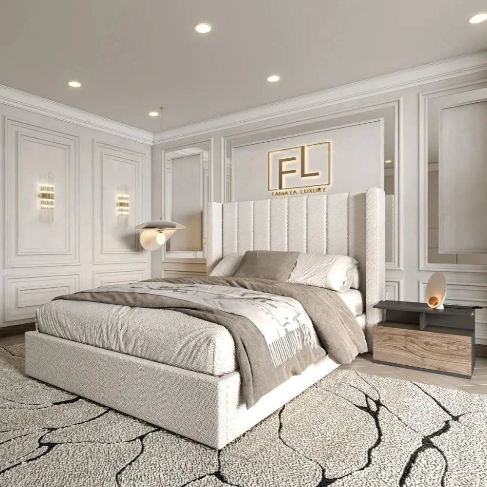 The image showcases The Manhattan Lined Wing Back Bed Frame in a luxurious bedroom with a neutral color palette. The large light gray upholstered bed features a tall textured headboard, matching pillows, and a light gray throw blanket. A plush area rug with abstract black lines complements the decor. A modern bedside table holds a decorative lamp. Intricate panel moldings enhance the room's sophistication, while the "FL" logo and "FAMAYA LUXURY" text are displayed above the bed. 