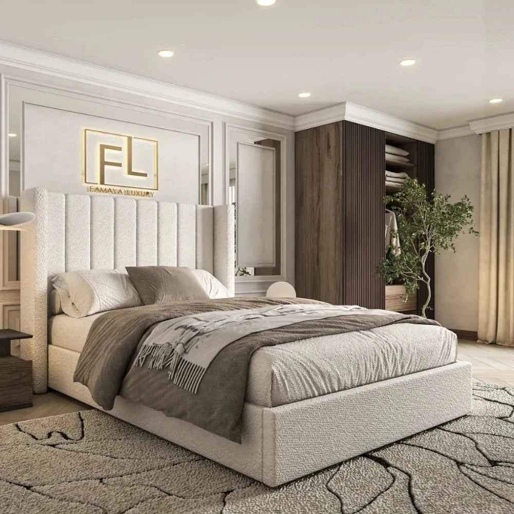 The image showcases The Manhattan Lined Wing Back Bed Frame in a modern bedroom. The plush bed features a high, vertically channeled off-white headboard and neutral bedding. Above it, a gold "FL" logo complements light off-white paneling. A wooden shelving unit displays neatly folded items and a green plant, while soft recessed lighting and an organic-patterned rug add warmth and texture to the space.