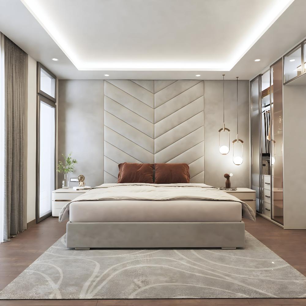 The image depicts a modern bedroom featuring a large, upholstered chevron grand panel bed with a plush grey headboard designed in a zigzag pattern. The bed is adorned with two brown pillows and a neatly spread beige duvet. On either side of the bed are sleek, white bedside tables. A gold table lamp and a small plant rest on the left bedside table, while the right side holds two decorative pendant lights hanging from the ceiling, casting a soft glow. 