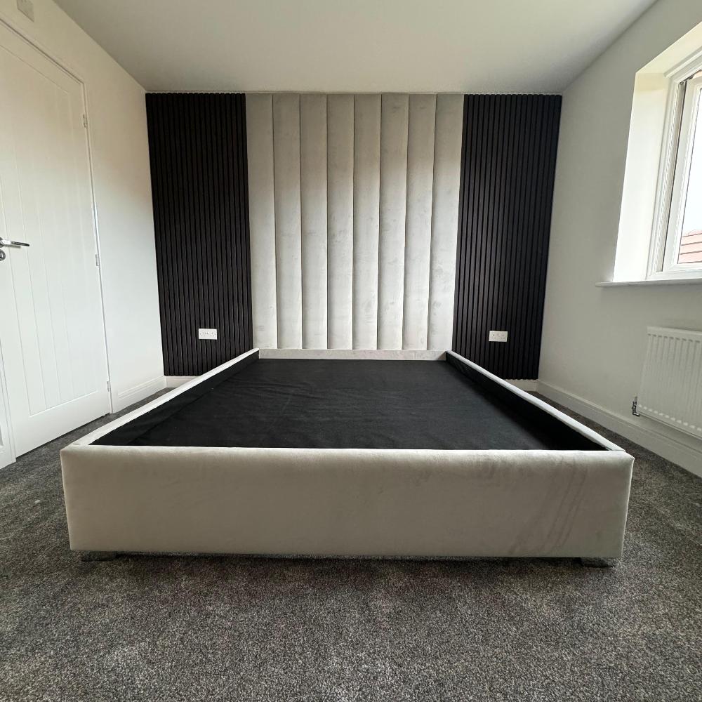 A modern bedroom with a bed frame against a wall with vertical gray and black aku panels and a window on the right.

