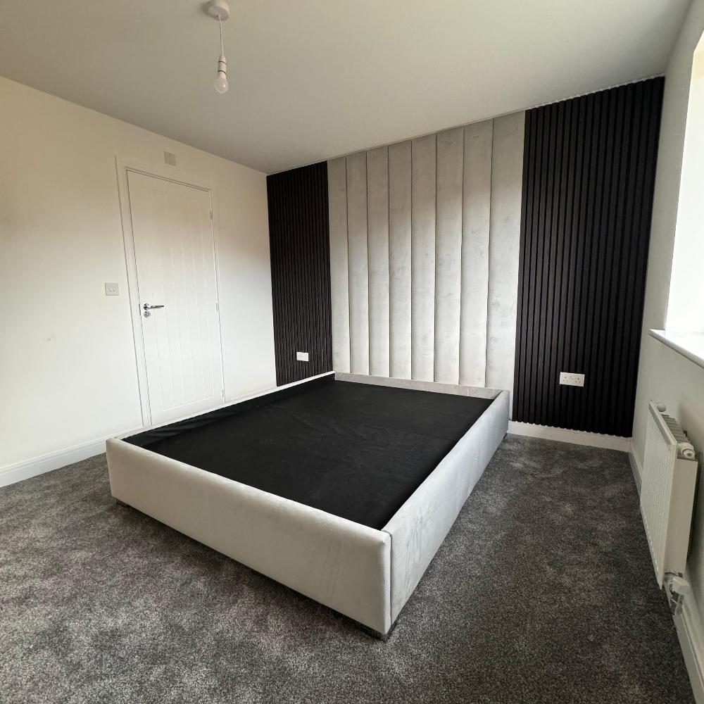 Modern bedroom with a bed frame, textured aku wall panels, and gray carpet.

