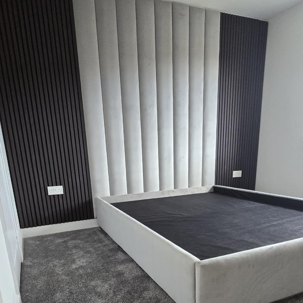 Modern bedroom with a light gray upholstered bed and a feature wall with alternating white and dark gray aku panels bed frame.

