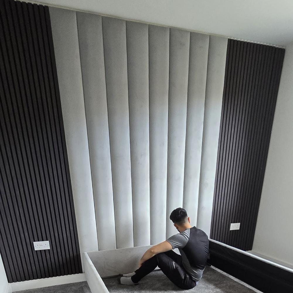 Person sitting on carpeted floor, facing a modern wall with gray padded and textured black aku panels.

