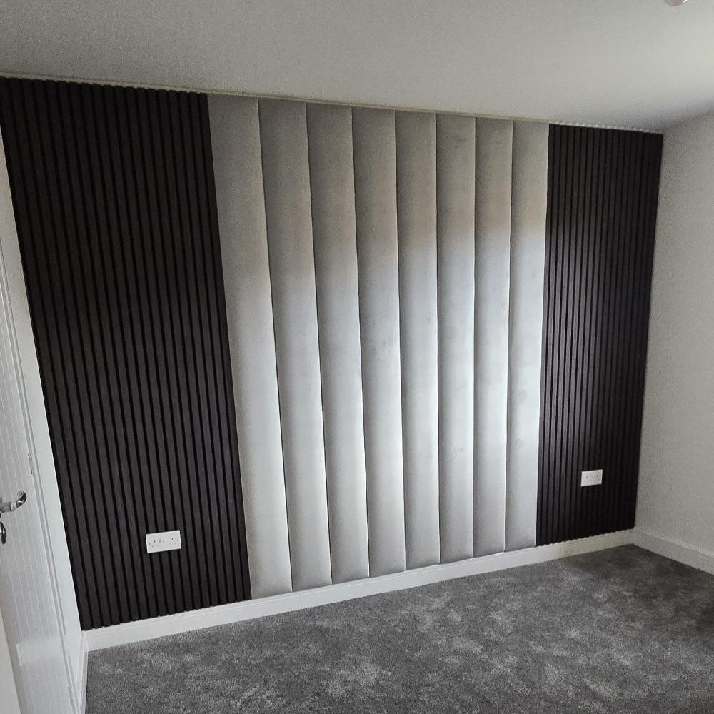 Room with a wall of vertical gray aku panels and dark slatted sections, light gray carpet floor, and a white door.

