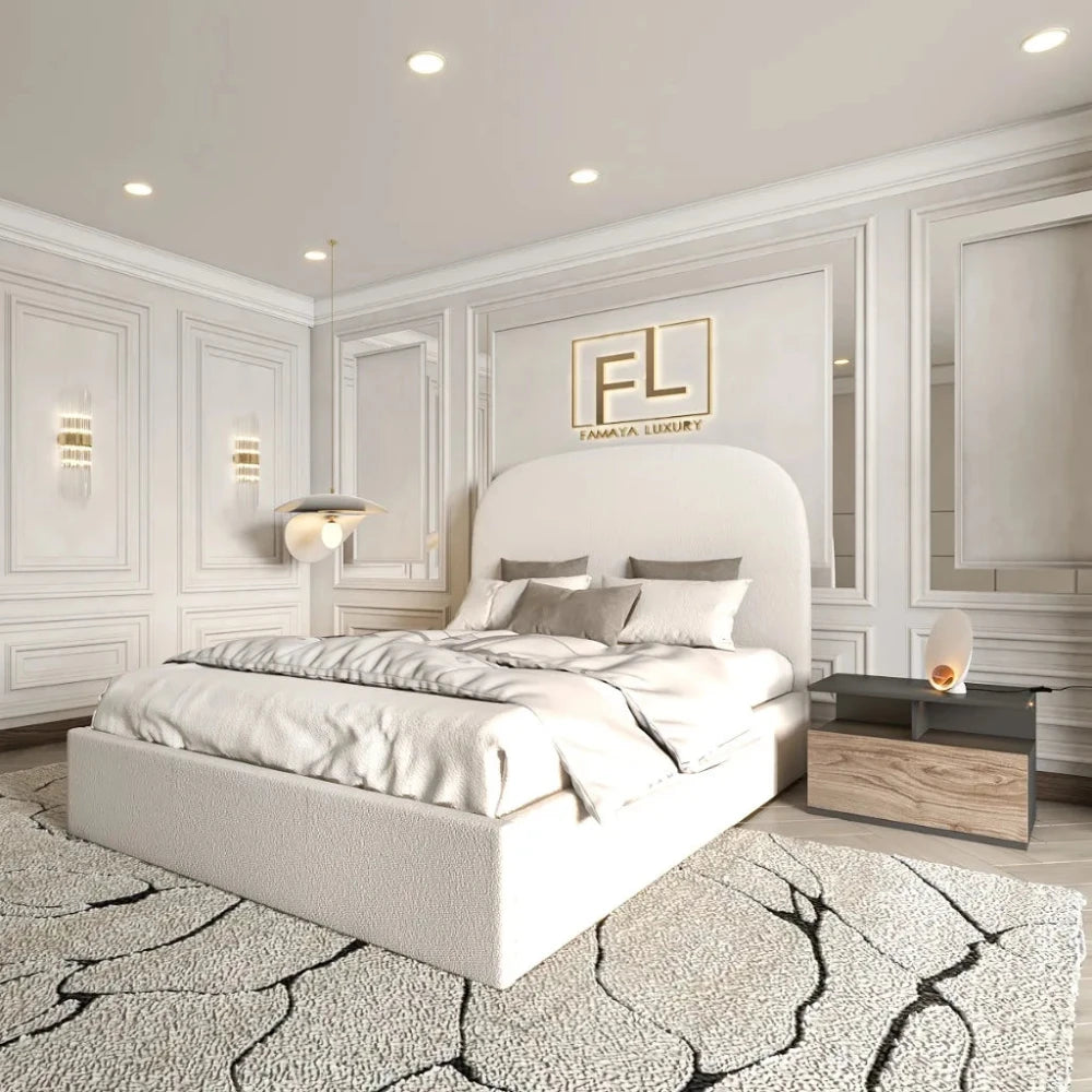 The image showcases a luxurious and modern bedroom centered around The Boucle Bed Frame upholstered in light cream fabric. The bed is adorned with plush gray and cream pillows, a matching blanket, and is set against a decorative wall panel featuring the gold "FL" logo and "FAMAYA LUXURY." Light gray paneled walls add sophistication, while a wooden nightstand with a sculptural lamp and a cracked-design rug enhance the elegant ambiance. A wall-mounted modern lamp and recessed ceiling lights complete the styli