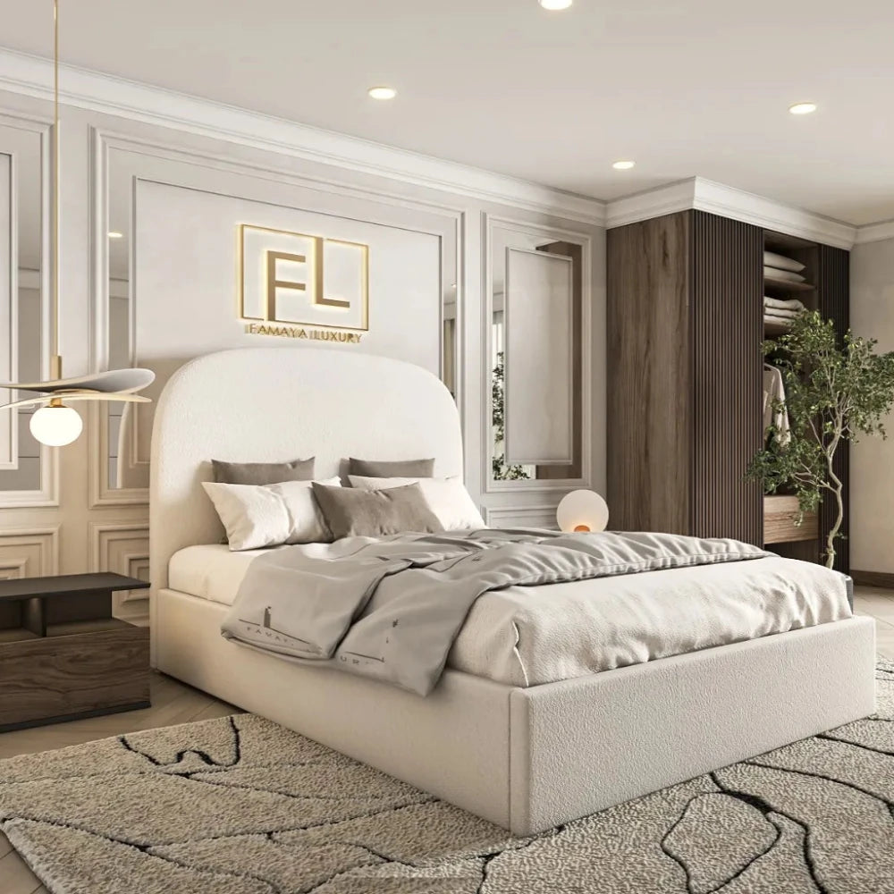 The image presents a contemporary bedroom with a neutral palette, centered around The Boucle Bed Frame with a tall, rounded headboard in soft beige fabric. The bed features neatly arranged pillows and a textured light gray blanket. To the left, a modern pendant light with a gold stem complements the plush aesthetic. A dark wooden bedside table and a patterned cream-beige carpet enhance the space. The back wall, adorned with decorative white paneling and inset mirrors, features a golden "FL FAMAYA LUXURY" .