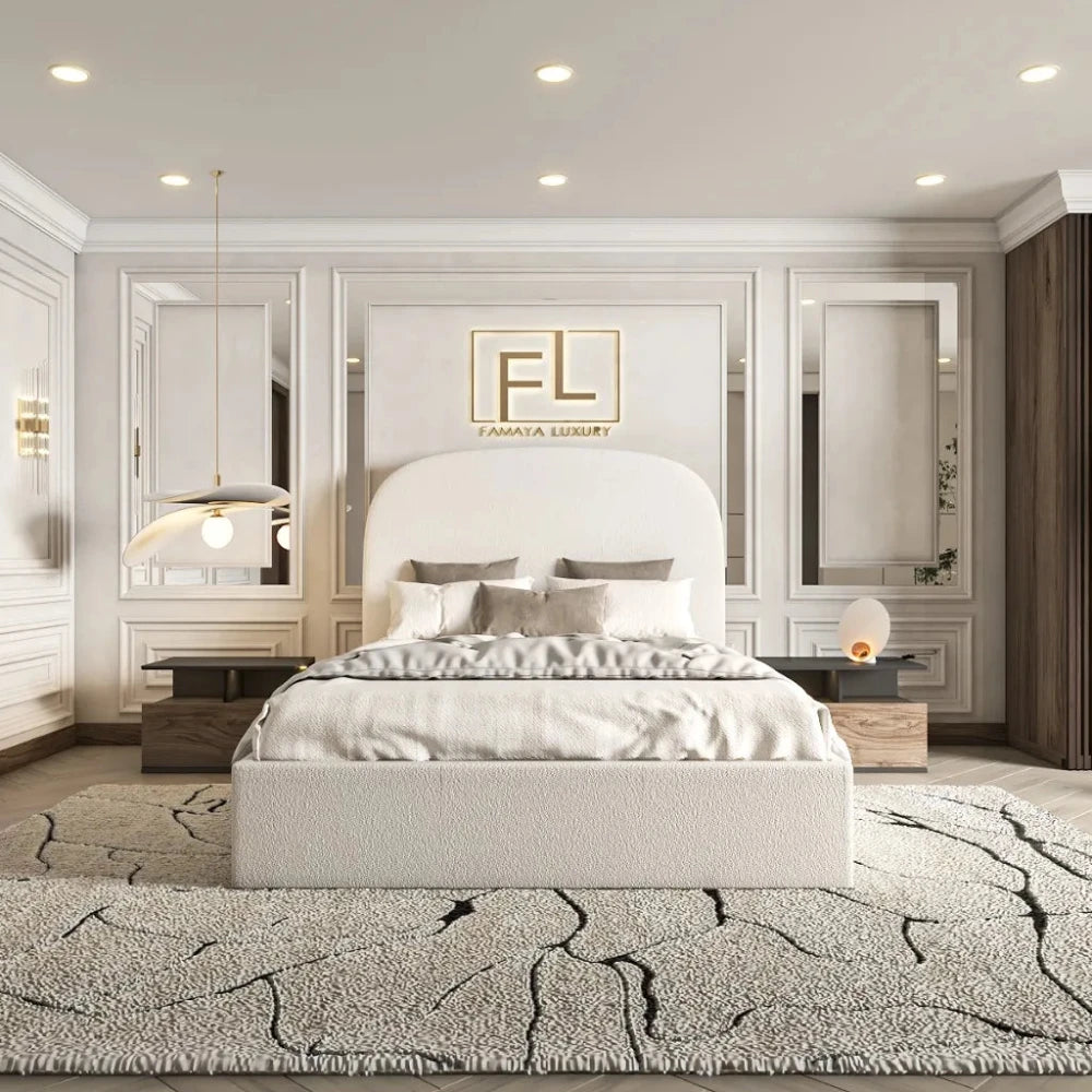 The image features a modern, luxurious bedroom centered around The Boucle Bed Frame with an arched headboard upholstered in white. The bed is styled with three square gray pillows and crisp white bedding. Two dark wooden bedside tables hold a spherical lamp and a pendant lamp with a bulbous shade. The wall behind is paneled in white with mirrored sections, adding depth. Above the headboard, a gold embossed logo accentuates the space. A plush, textured rug in gray and charcoal completes the serene.