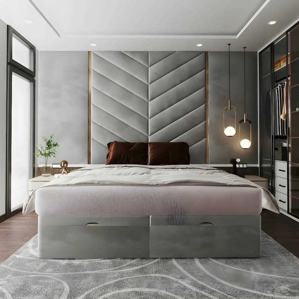 The image depicts a modern bedroom interior with a minimalist design. The focal point is a large chevron grand panel bed with a grey fabric headboard featuring a chevron pattern, flanked by vertical wooden panels. The bed is dressed in white sheets with dark tan pillows. Beneath the bed is a large, grey base with two visible drawers. The room features a muted color palette predominantly in shades of grey and brown. 