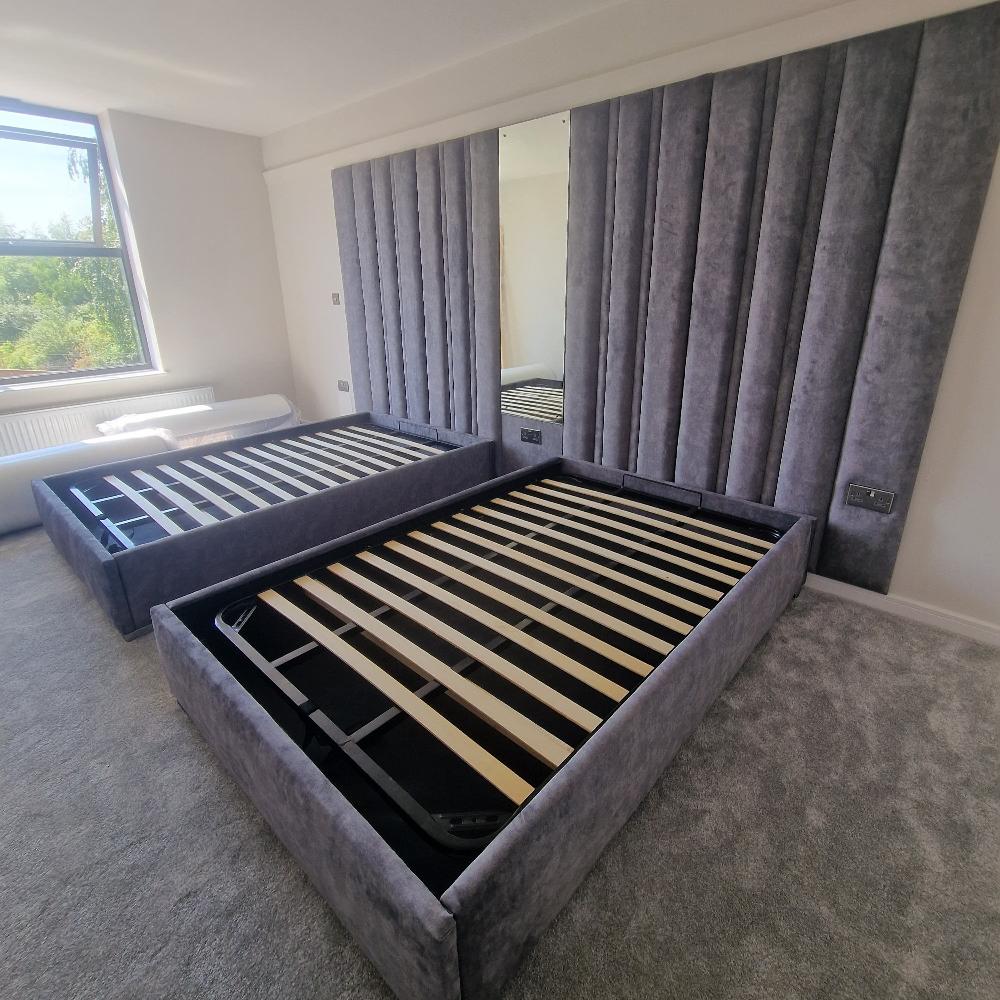 Two duo panel bed frames with gray upholstered headboards and a central mirror in a carpeted bedroom.

